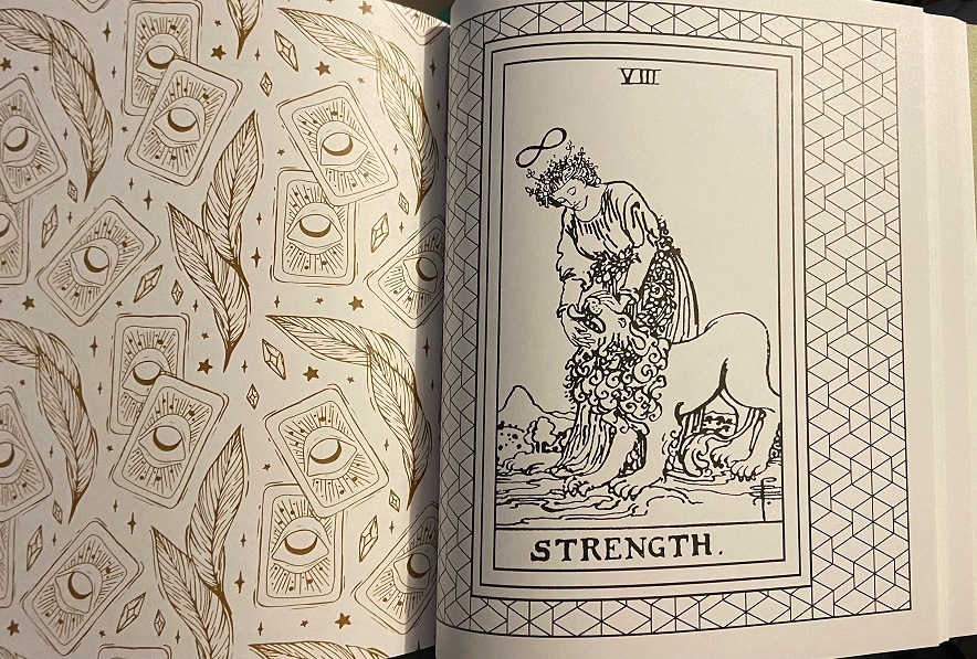 On the left page is a gold-tone pattern of eyes in cards.  On the right is an illustration of the tarot card Strength.