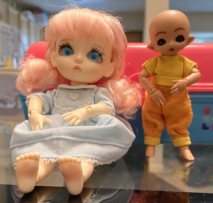 Candy, a doll in a blue Victorian dress with pink hair, and Thimble, a bald tan-skinned doll in yellow and orange clothing.